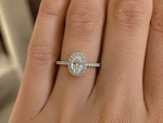 Load image into Gallery viewer, Oval halo natural diamond engagement ring in white gold, shown on a woman’s hand in natural light.