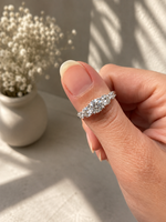 Load image into Gallery viewer, Five-stone natural diamond ring in white gold with graduated round brilliant diamonds, shown on a woman’s hand against a soft, realistic lifestyle background.