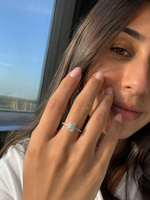 Load image into Gallery viewer, Emerald halo natural diamond engagement ring on a woman’s hand in a natural lifestyle portrait, featuring a delicate pavé band and elegant halo setting.