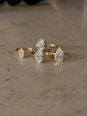 Four natural diamond solitaire rings in yellow gold featuring three oval-cut diamonds and one pear-shaped diamond in different setting styles.