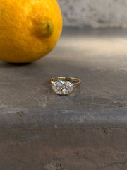 Oval natural diamond bezel-set solitaire ring in yellow gold on concrete surface with citrus background
