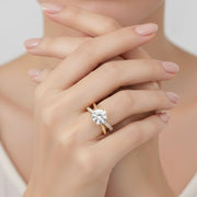 Model hand wearing round diamond engagement ring featuring pavé band and X-style split shank, close-up on soft neutral background