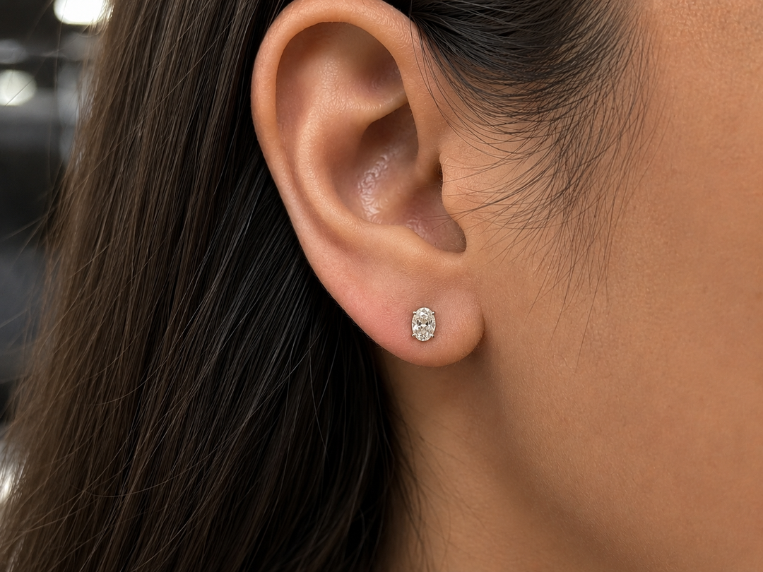 Oval cut lab grown diamond stud earring worn on ear in yellow gold, classic solitaire setting