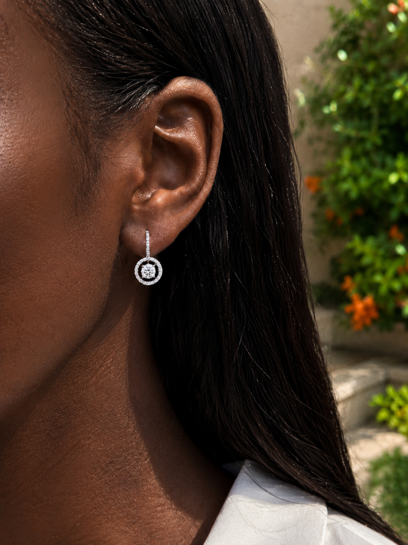     Close-up of a woman wearing a white gold natural diamond drop earring with a circular double-halo design and diamond-covered hook.