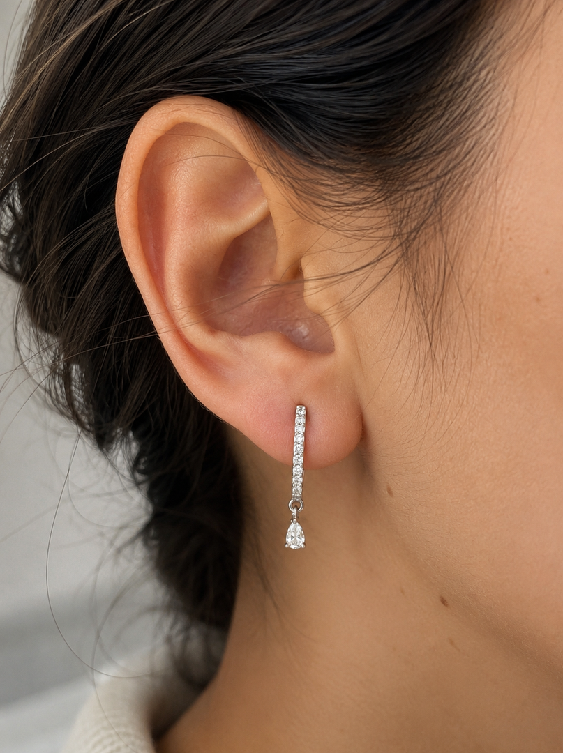 Lab-grown diamond raindrop earrings in white gold, featuring pavé-set huggie hoops with dangling pear-shaped diamonds, shown on a woman’s ear.