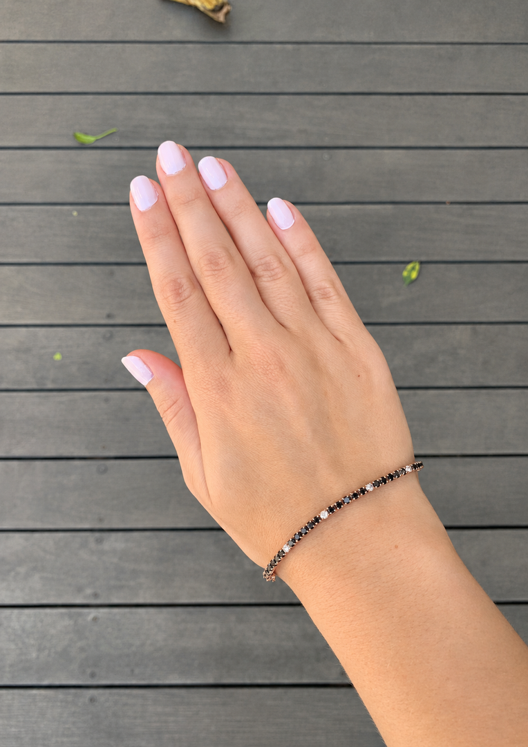 Natural Black & White Diamond Tennis Bracelet in White Gold Worn on a Woman’s Wrist, Showcasing Alternating Round Black and White Diamonds in an Elegant Tennis Bracelet Style.
