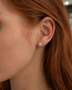 Load image into Gallery viewer, Round natural diamond stud earring worn on ear, classic solitaire setting with a single brilliant-cut diamond, minimalist fine jewelry close-up.