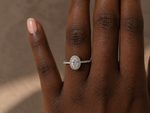 Load image into Gallery viewer,     Oval halo lab-grown diamond engagement ring in white gold, shown on a woman’s hand in natural light.