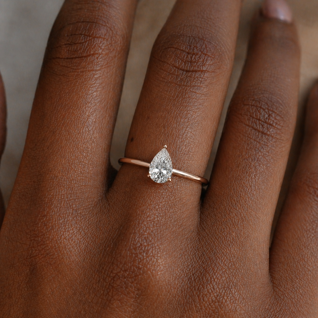 Lab grown pear cut diamond hidden halo engagement ring worn on a hand in 18K rose gold