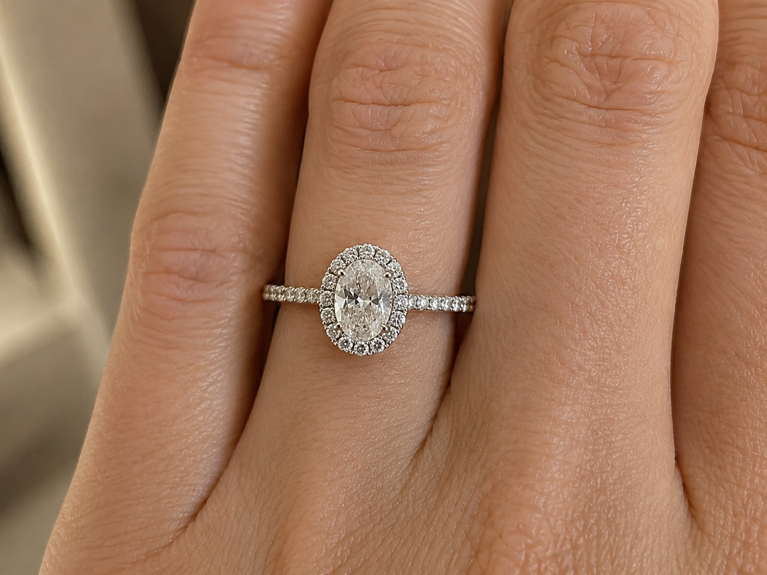     Oval halo natural diamond engagement ring in white gold, shown on a woman’s hand in natural light.