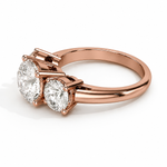 Load image into Gallery viewer, Angled view of a three stone round natural diamond engagement ring in rose gold on a white background.