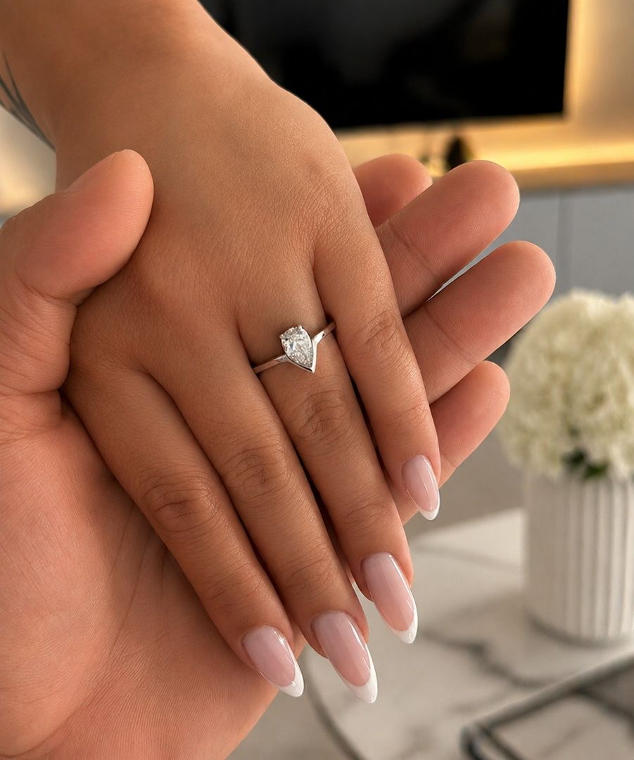 Close-up of a woman’s hand wearing a fifty fifty pear shape lab-grown diamond ring, gently held by a man’s hand.