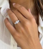Load image into Gallery viewer, Three stone round natural diamond engagement ring in white gold worn on a woman’s hand in natural light.