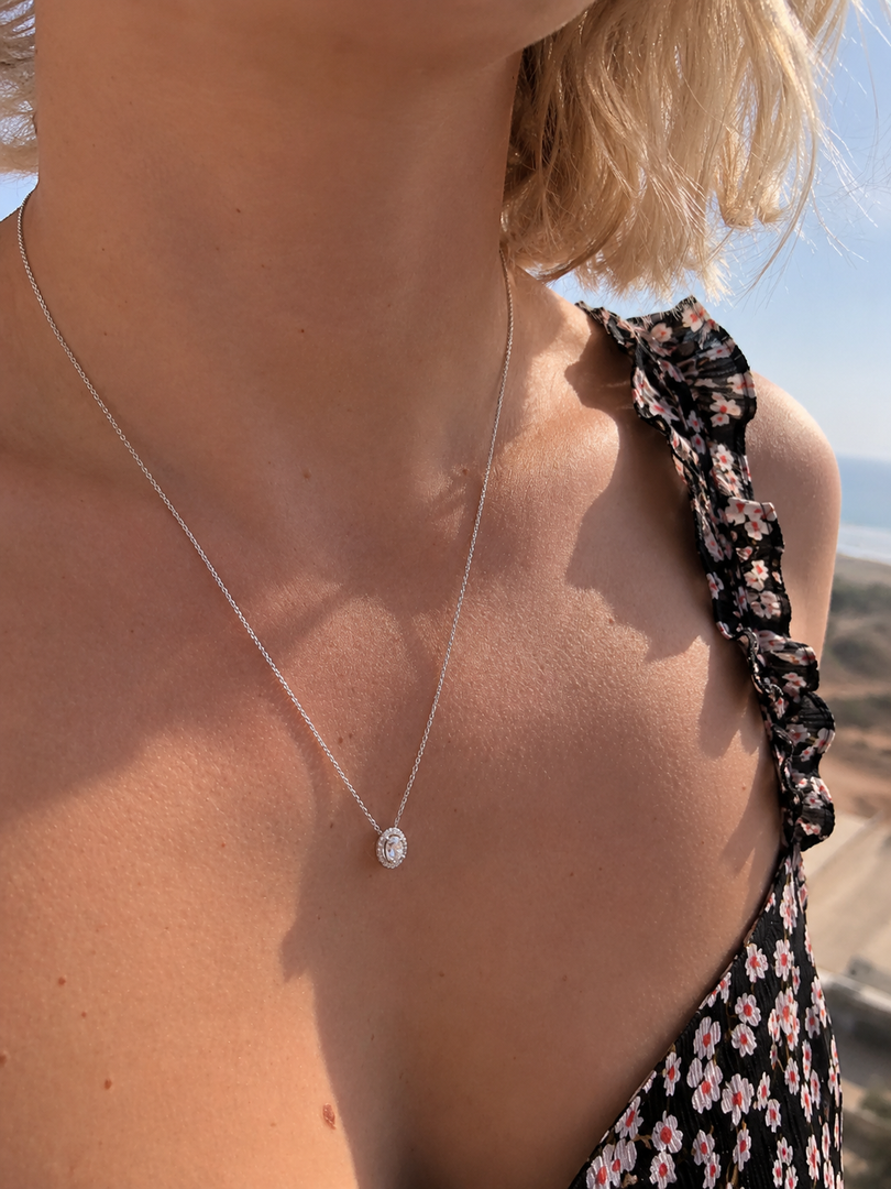 Natural round halo diamond pendant necklace worn by a woman in white gold with a delicate chain and timeless everyday style.