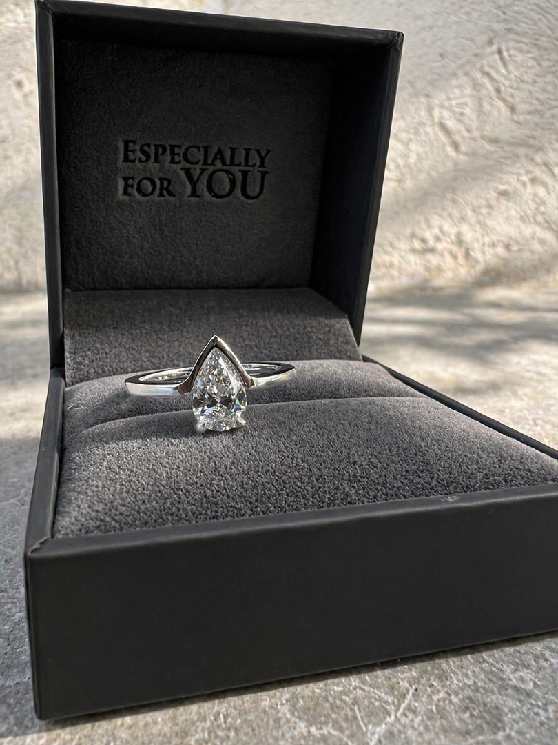 Close-up of a fifty fifty pear shape natural diamond ring displayed inside an open ring box.