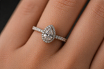 Load image into Gallery viewer, Pear-shaped natural diamond engagement ring in white gold with a diamond halo, shown on hand