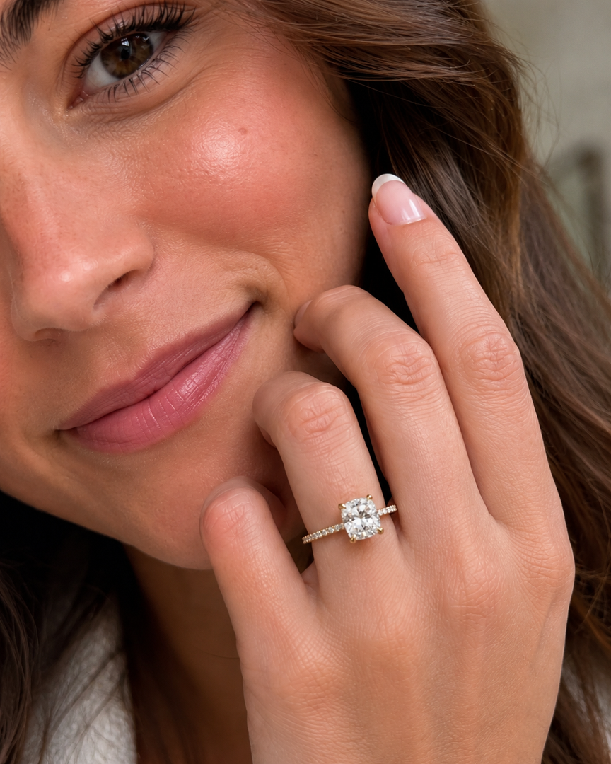 Woman wearing a natural cushion-cut solitaire engagement ring with pavé diamonds along the band.