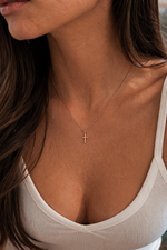 Load image into Gallery viewer, Delicate gold cross necklace with a fine chain and small polished cross pendant, worn on a woman’s neck for a minimalist and timeless look.