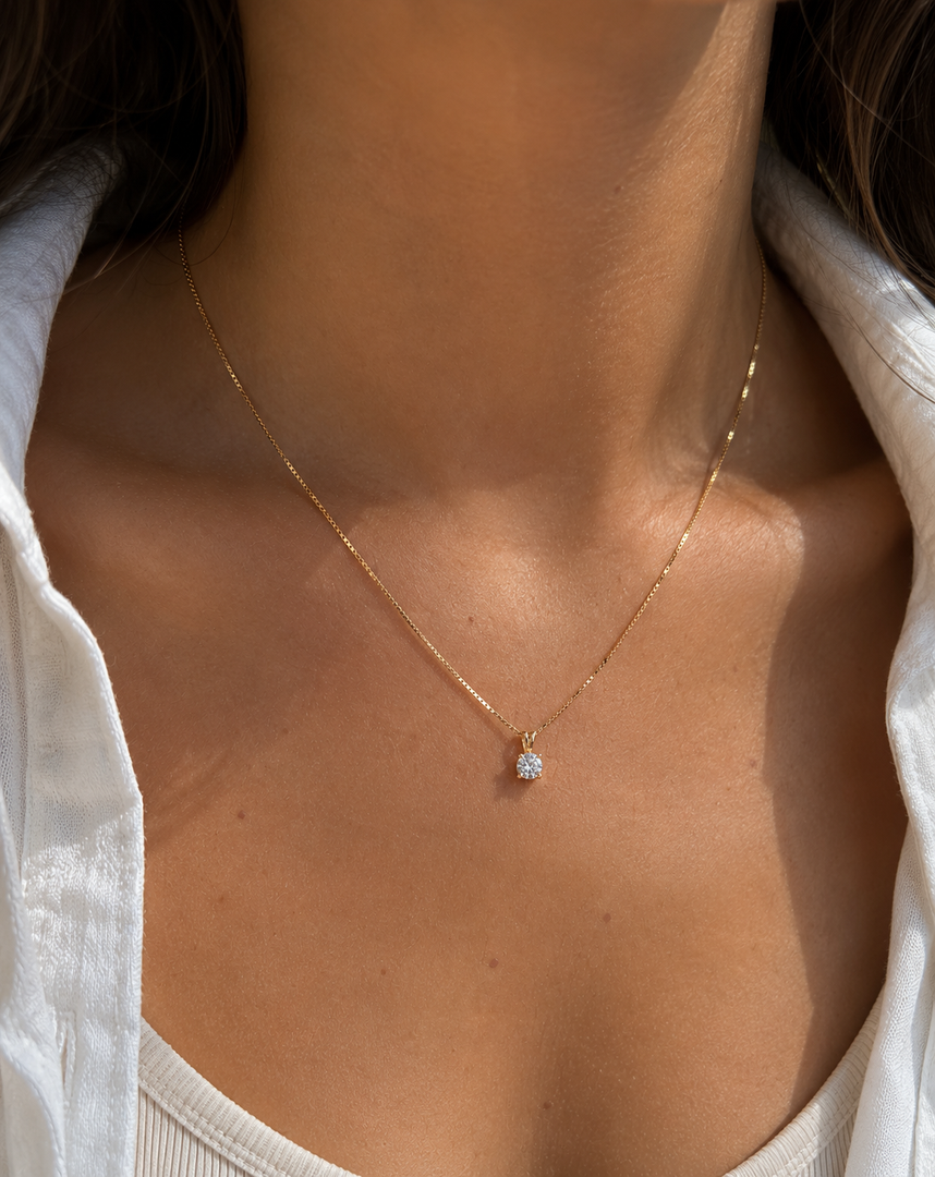 Round lab-grown diamond solitaire pendant necklace in yellow gold on a woman’s neck, delicate thin gold chain, close-up jewelry photo