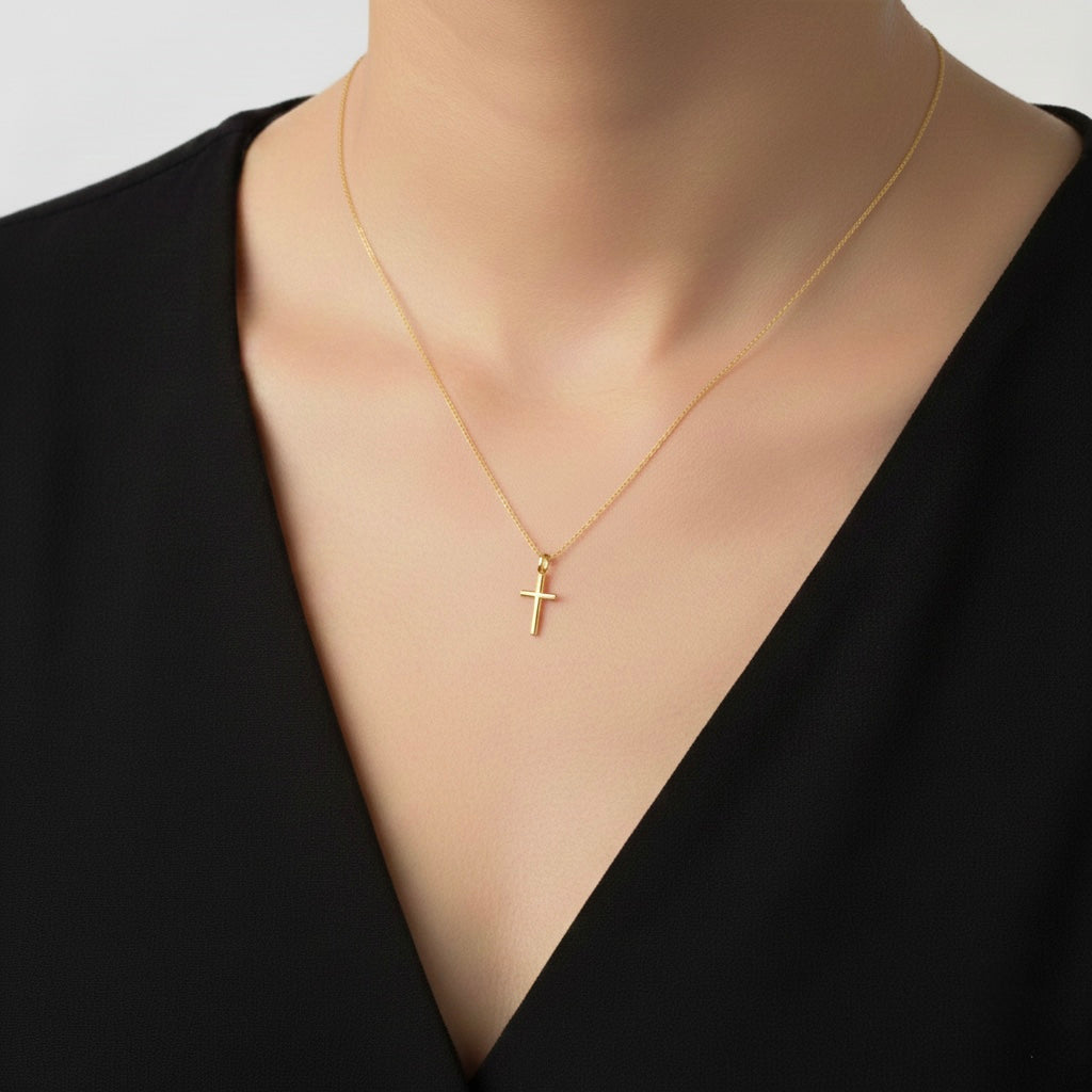 Delicate gold cross necklace with a fine chain and small polished cross pendant, worn on a woman’s neck for a minimalist and timeless look.