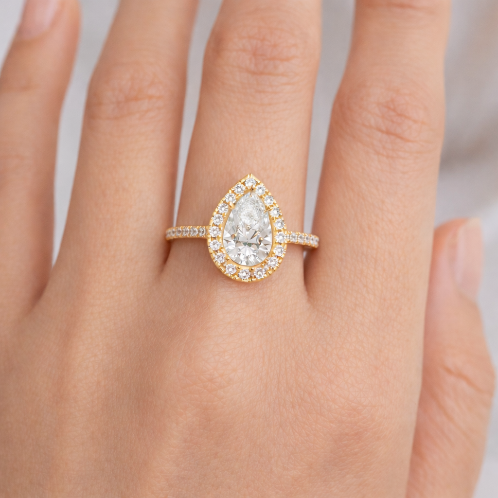 Pear-shaped natural diamond engagement ring in yellow gold with a diamond halo, shown on hand