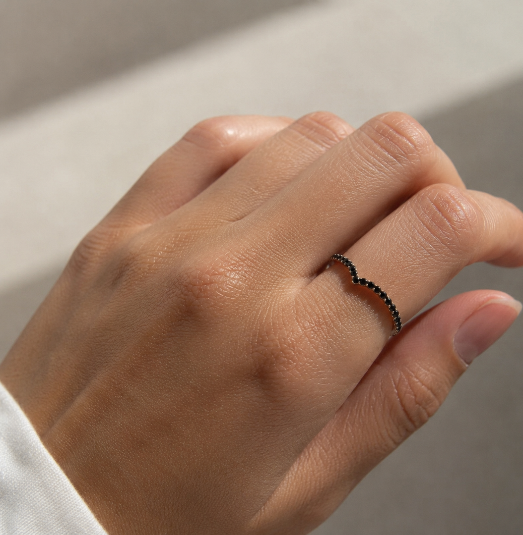 Close-up of a V-shape half eternity black diamond ring on a woman’s hand in natural sunlight.