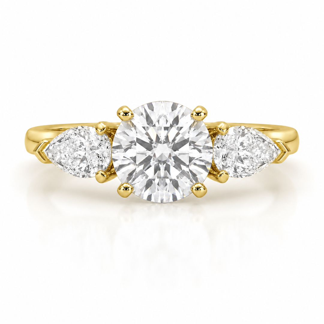 Three stone lab-grown diamond engagement ring with a round center diamond and pear side diamonds in yellow gold on a white background.