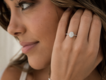 Load image into Gallery viewer, Close-up of a woman wearing an oval halo natural diamond engagement ring in white gold with an oval center diamond surrounded by round accent diamonds.