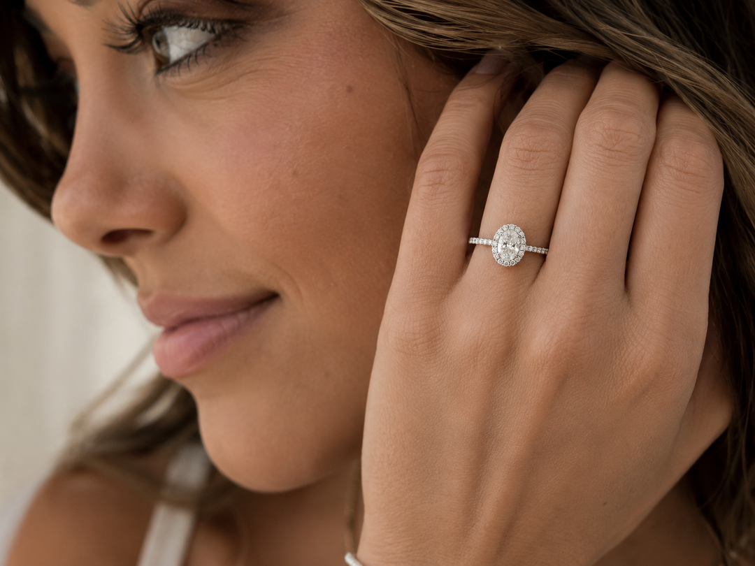 Close-up of a woman wearing an oval halo natural diamond engagement ring in white gold with an oval center diamond surrounded by round accent diamonds.