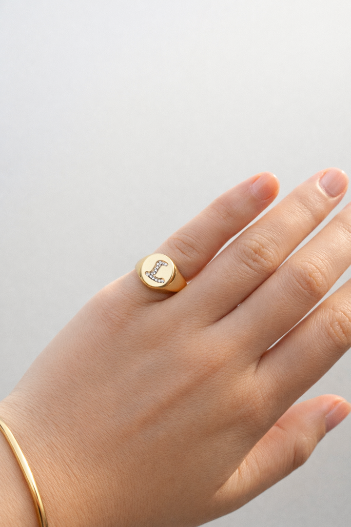 Natural diamond initial signet ring in yellow gold, round-cut diamonds, letter L detail, shown on hand against a soft neutral background