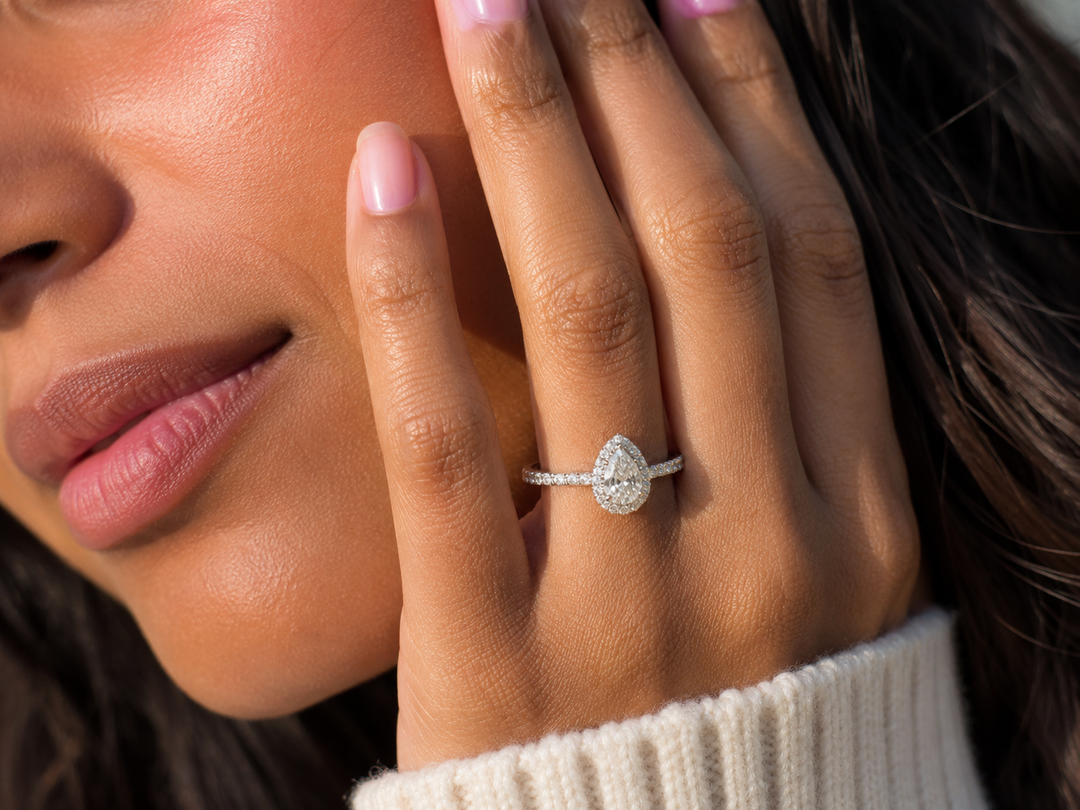 Close-up of a woman wearing a lab-grown pear halo diamond engagement ring with a pavé band.