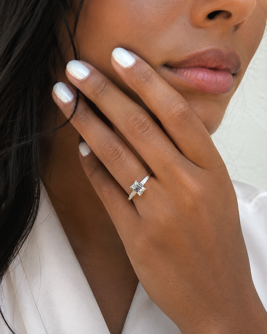 Natural emerald cut diamond ring with tapered side stones in yellow gold – lifestyle hand view